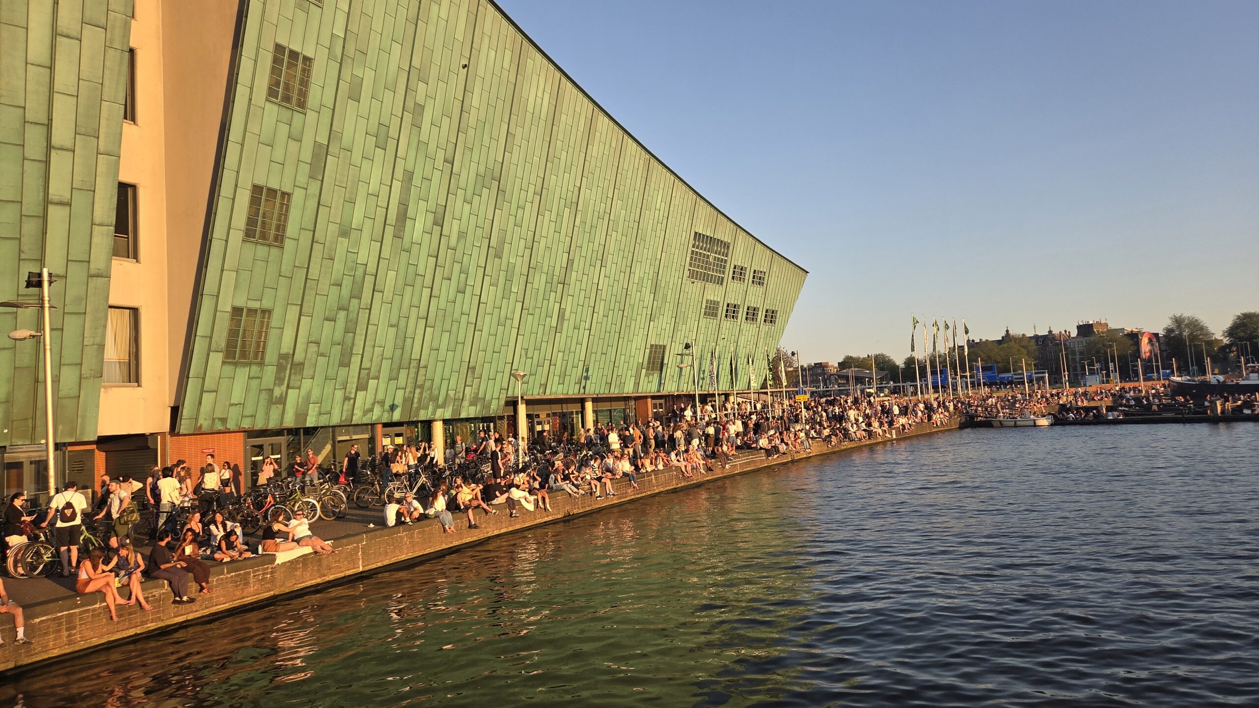 Warga duduk di pinggir sungai dengan latar belakang gedung Nemo Museum Amsterdam (Foto: Hengky Kurniawan).